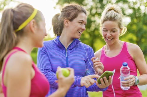 Women exercising outside looking at social site on mobile phone.